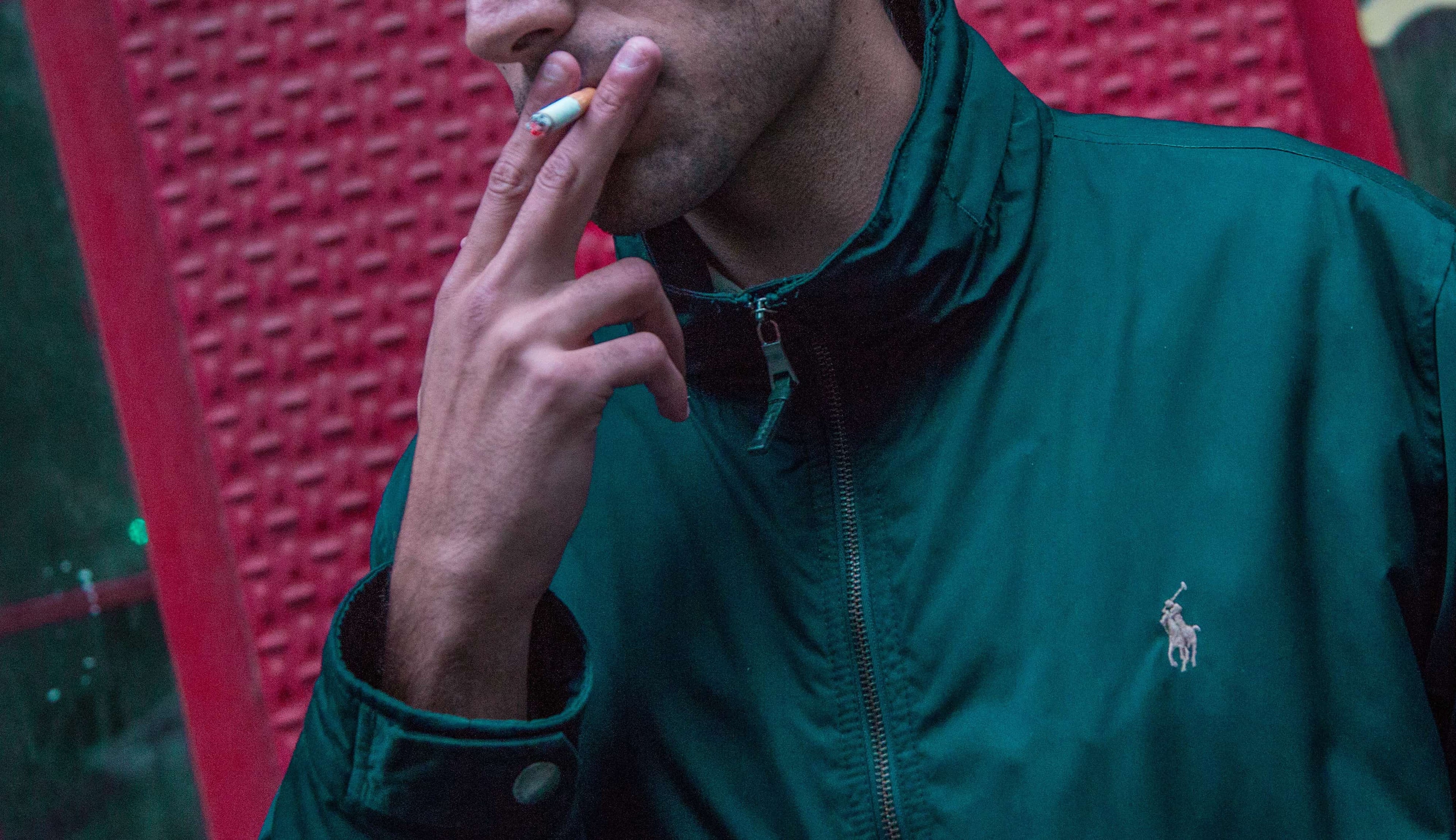 man in green teal color ralph lauren track jacket smoking a cigarette